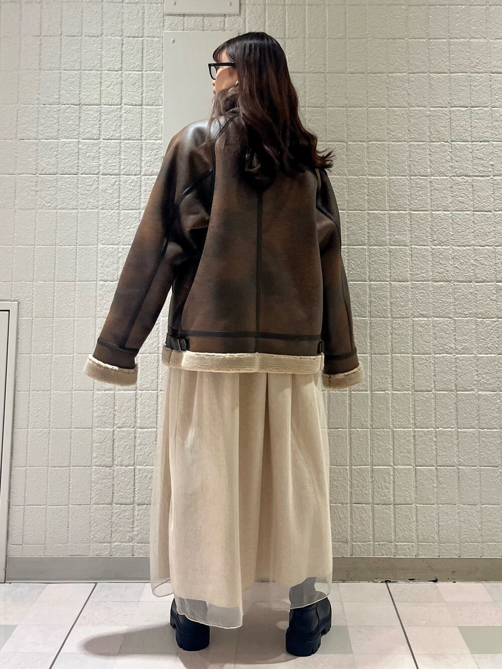 ブラウン系のムートンコート、ベージュ系のワンピース、ブラック系のブーツを着用したレディースの春コーディネートの4枚目の写真