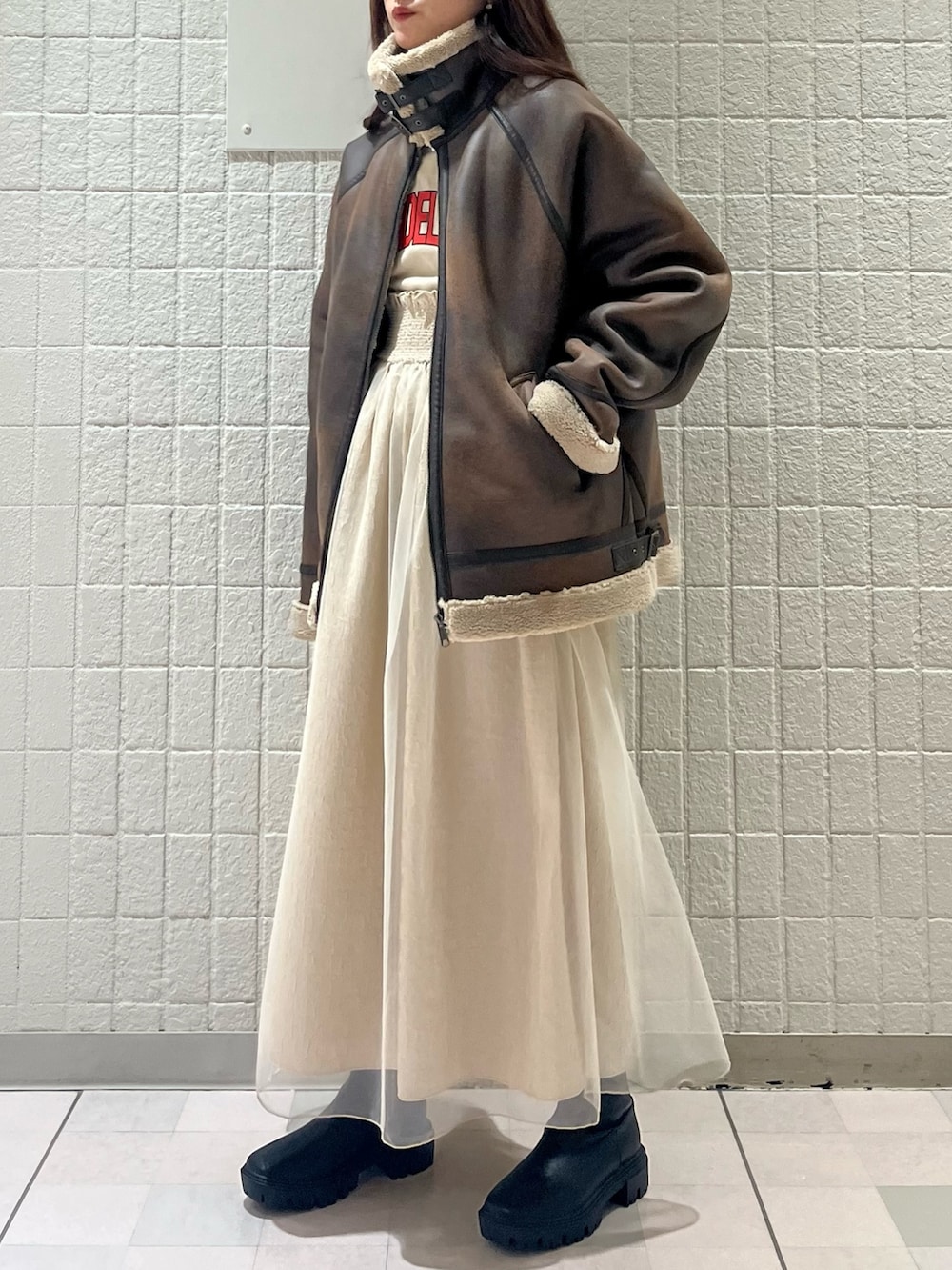 ブラウン系のムートンコート、ベージュ系のワンピース、ブラック系のブーツを着用したレディースの春コーディネートの3枚目の写真