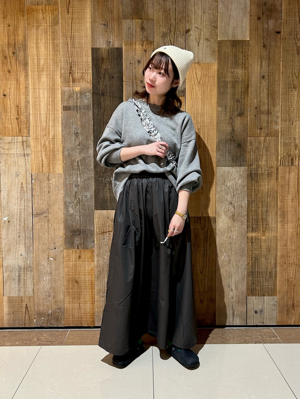 グレー系のニット/セーター、グレー系のスカート、シルバー系のショルダーバッグを着用したレディースの冬コーディネートの2枚目の写真