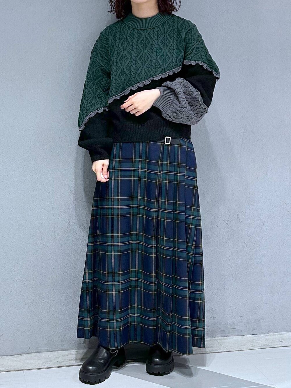 ブラック系のブーツ、グリーン系のスカート、ブラック系のニット/セーターを着用したレディースの秋コーディネートの2枚目の写真