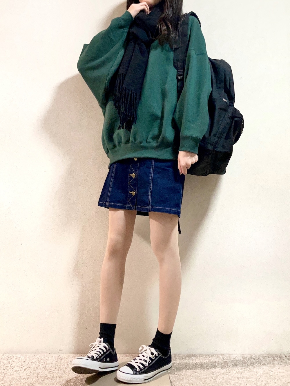 グリーン系のスウェット、ブラック系のバックパック/リュック、ブルー系のデニムスカートを着用したレディースの秋コーディネートの2枚目の写真