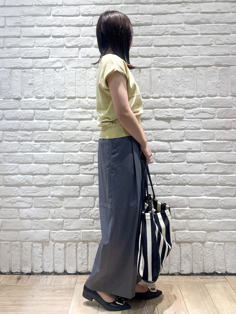 イエロー系のニット/セーター、グレー系のその他パンツ、ブラック系のトートバッグを着用したレディースの夏コーディネートの2枚目の写真