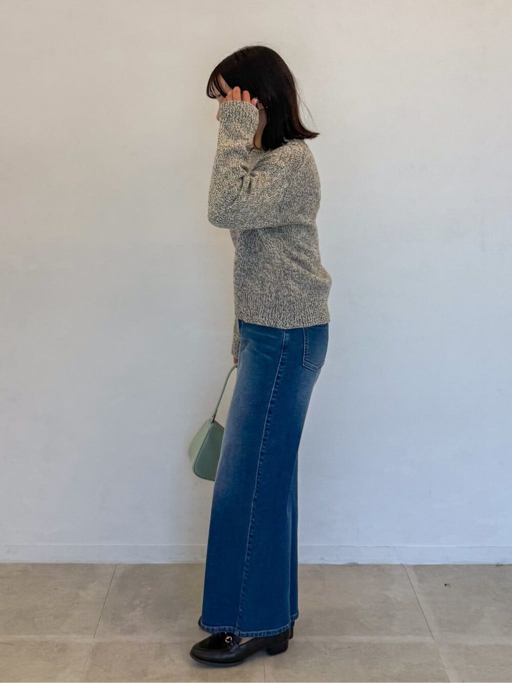 イエロー系のニット/セーター、ブルー系のデニムパンツ、グリーン系のショルダーバッグを着用したレディースの春コーディネートの2枚目の写真