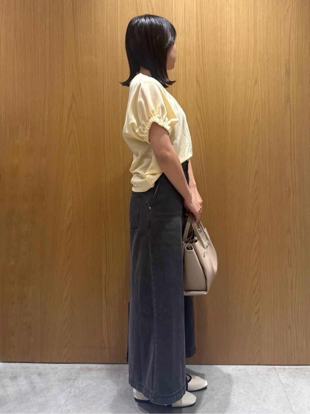 イエロー系のTシャツ/カットソー、ブラック系のデニムスカート、ベージュ系のショルダーバッグを着用したレディースの夏コーディネートの2枚目の写真