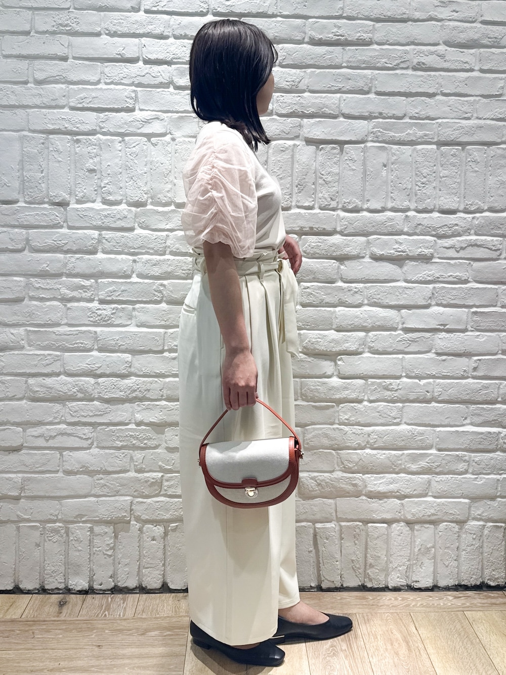 ブラック系のパンプス、レッド系のショルダーバッグ、オレンジ系のニット/セーターを着用したレディースの春コーディネートの2枚目の写真