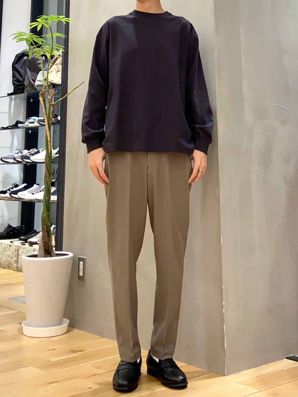 グリーン系のステンカラーコート、グレー系のTシャツ/カットソー、ブラック系のトートバッグを着用したメンズの春コーディネートの3枚目の写真