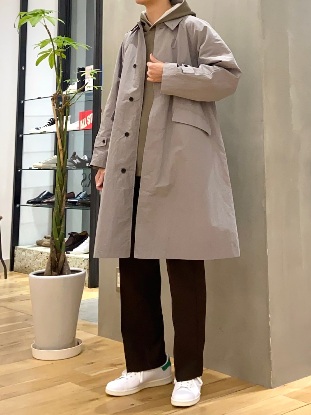 グレー系のステンカラーコート、グリーン系のパーカー、ブラウン系のその他パンツを着用したメンズの春コーディネートの3枚目の写真