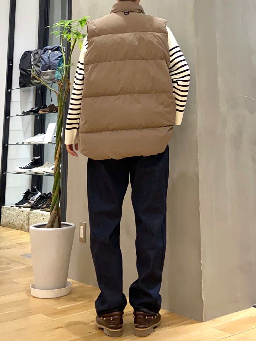 ブラウン系のダウンベスト、ホワイト系のニット/セーター、ブルー系のデニムパンツを着用したメンズの秋コーディネートの3枚目の写真