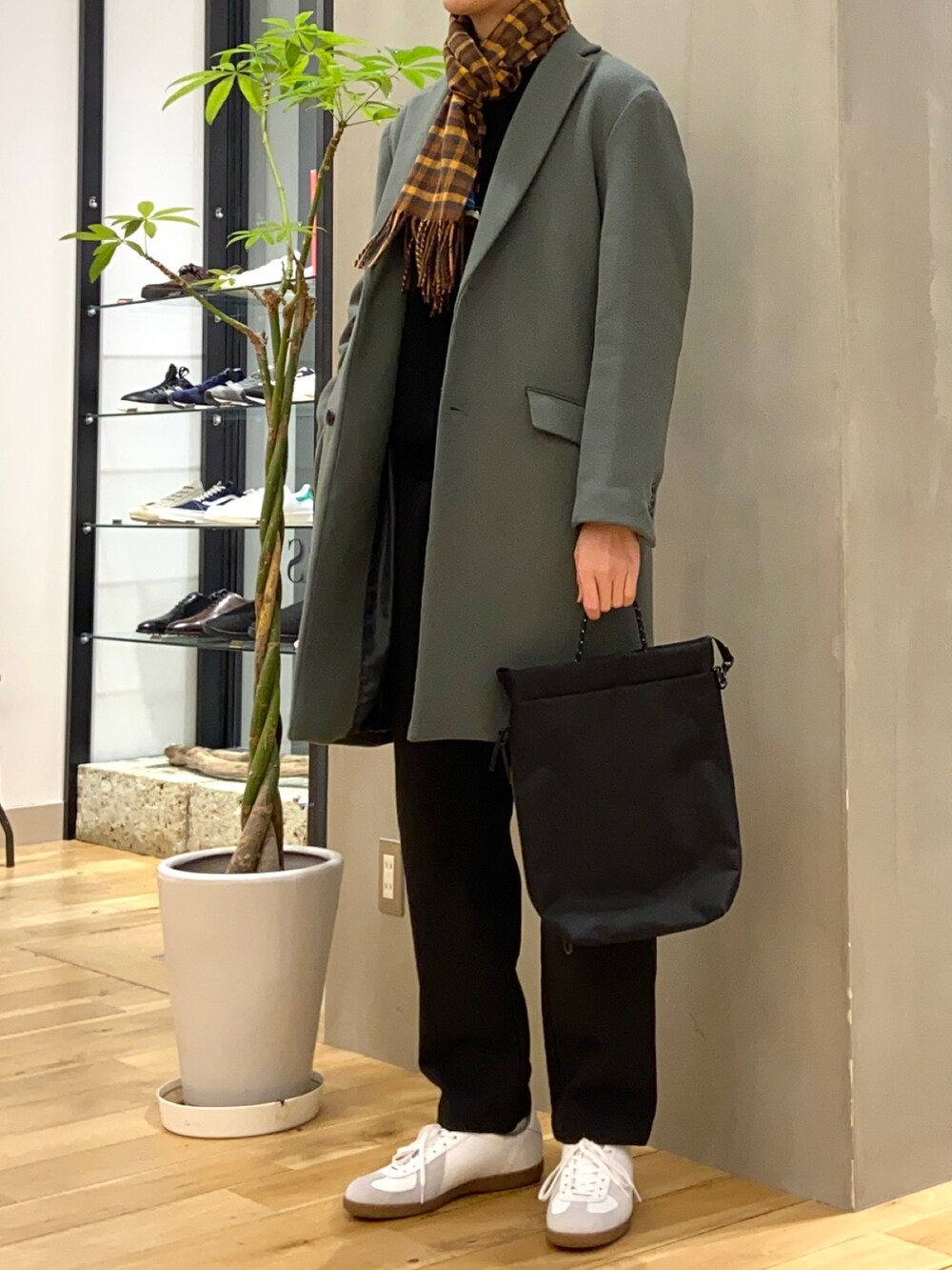 グリーン系のチェスターコート、ブラック系のその他パンツ、ホワイト系のスニーカーを着用したメンズの冬コーディネートの2枚目の写真