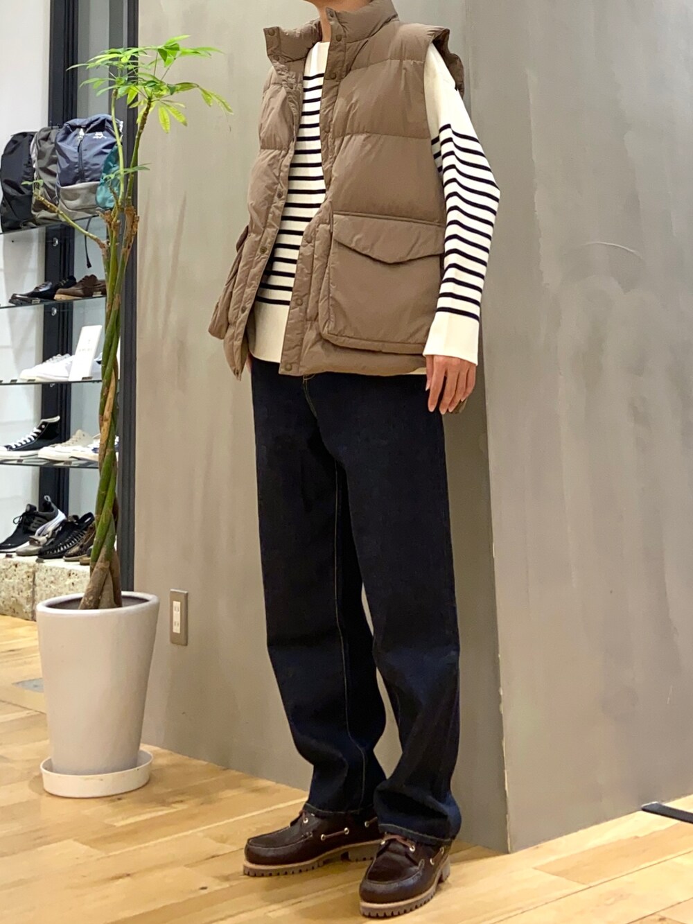 ブラウン系のダウンベスト、ホワイト系のニット/セーター、ブルー系のデニムパンツを着用したメンズの秋コーディネートの2枚目の写真