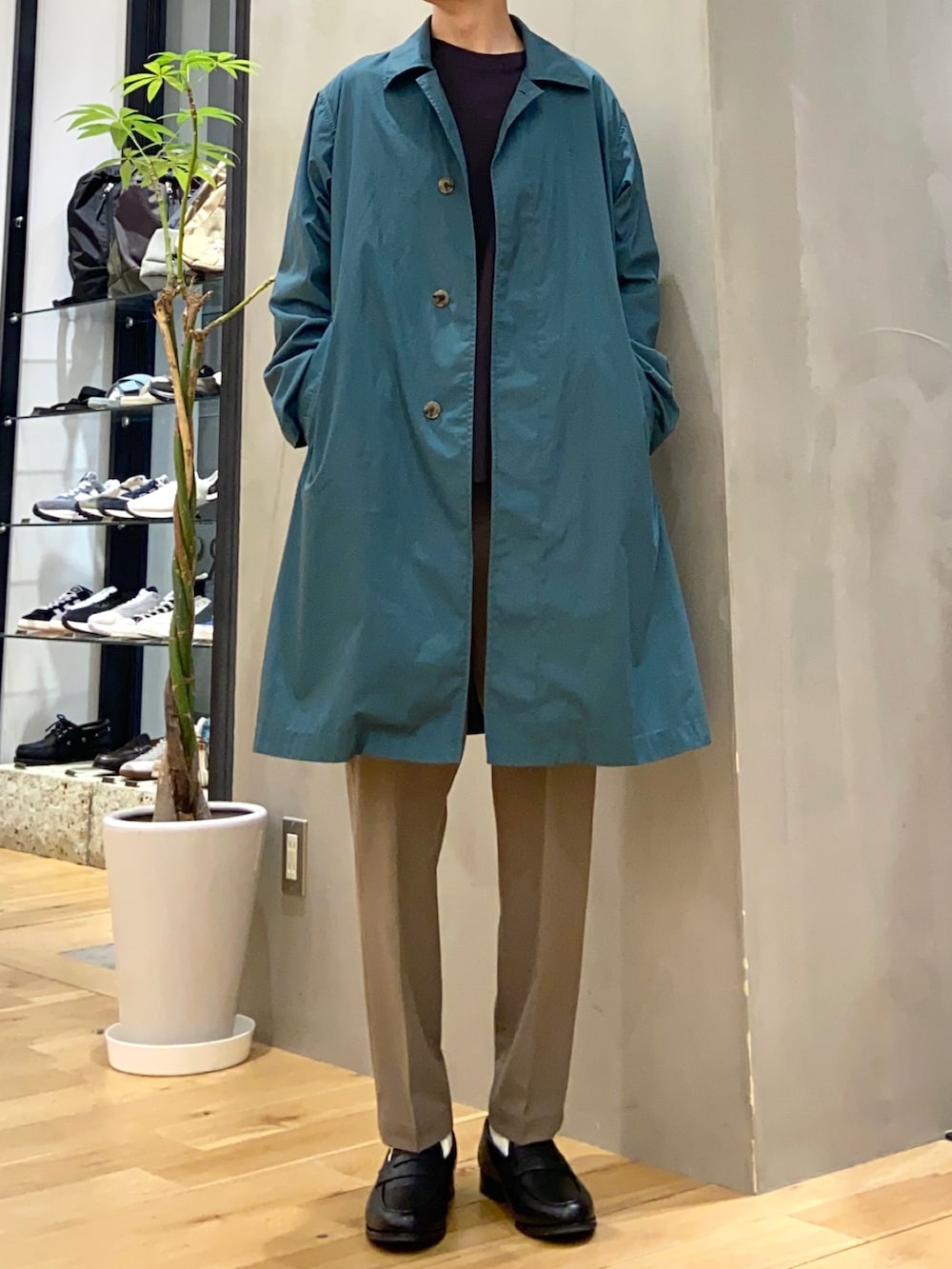 グリーン系のステンカラーコート、グレー系のTシャツ/カットソー、ブラック系のトートバッグを着用したメンズの春コーディネートの4枚目の写真