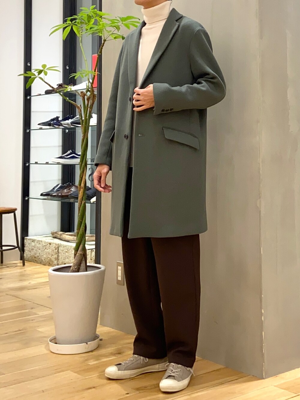 グリーン系のチェスターコート、ホワイト系のニット/セーター、グレー系のスニーカーを着用したメンズの冬コーディネートの4枚目の写真