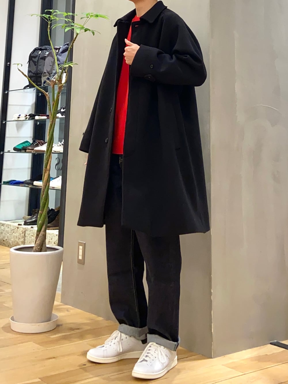 ブラック系のステンカラーコート、レッド系のニット/セーター、ブルー系のデニムパンツを着用したメンズの冬コーディネートの3枚目の写真