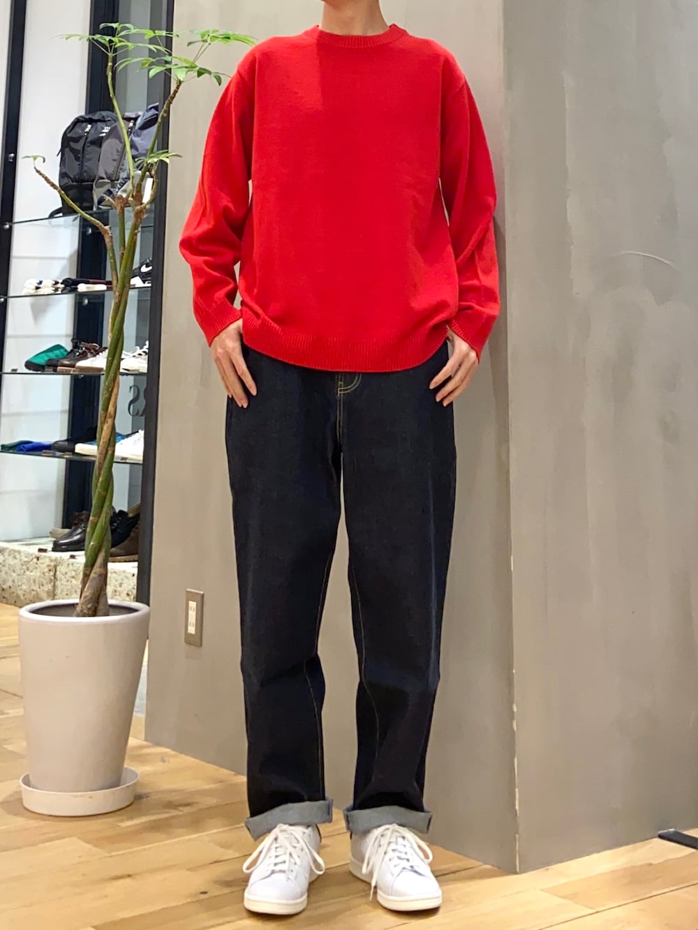 ブラック系のステンカラーコート、レッド系のニット/セーター、ブルー系のデニムパンツを着用したメンズの冬コーディネートの2枚目の写真