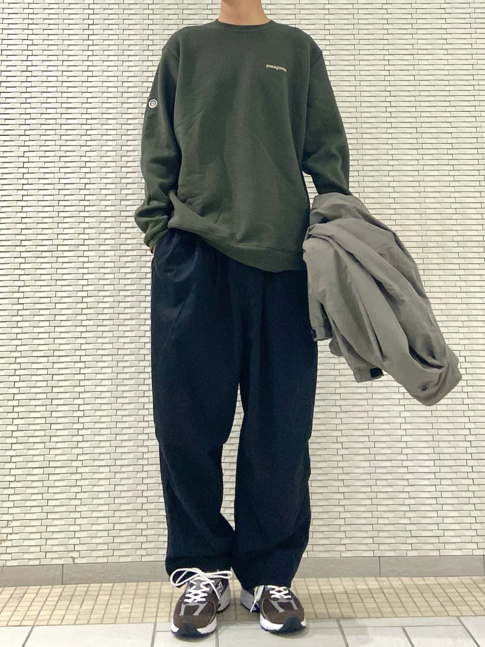 グレー系のブルゾン、ブラック系のチノパンツ、ブラウン系のスニーカーを着用したメンズの秋コーディネートの3枚目の写真