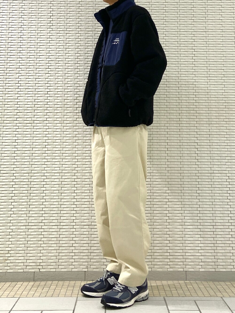 ブラック系のブルゾン、ホワイト系のチノパンツ、ブルー系のスニーカーを着用したメンズの秋コーディネートの2枚目の写真