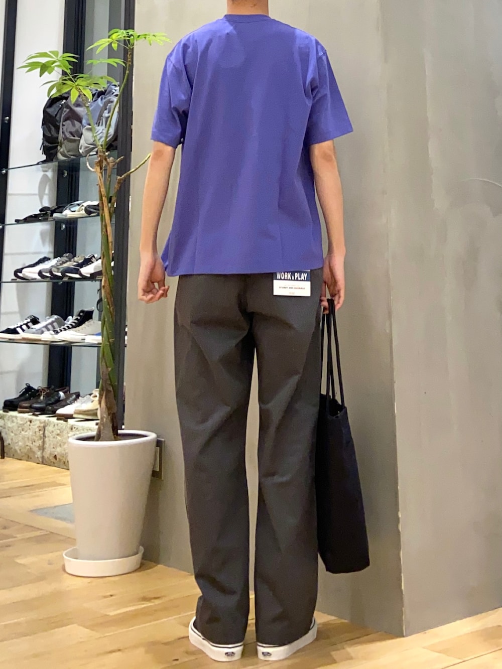 ブラック系のトートバッグ、ブラック系のスニーカー、パープル系のTシャツ/カットソーを着用したメンズの春コーディネートの3枚目の写真