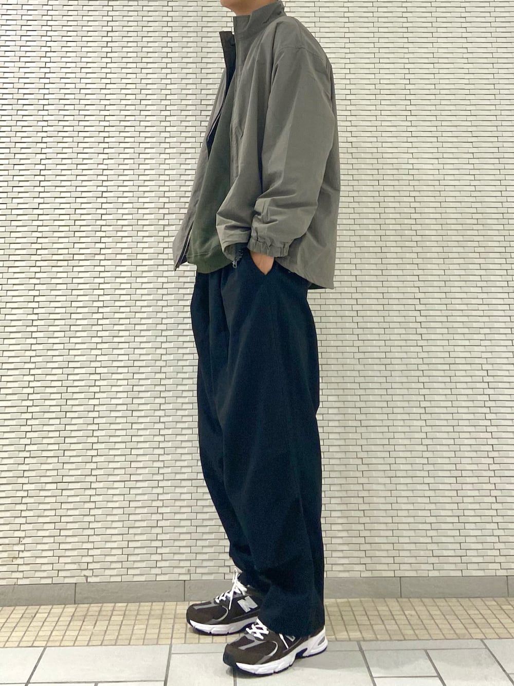 グレー系のブルゾン、ブラック系のチノパンツ、ブラウン系のスニーカーを着用したメンズの秋コーディネートの2枚目の写真