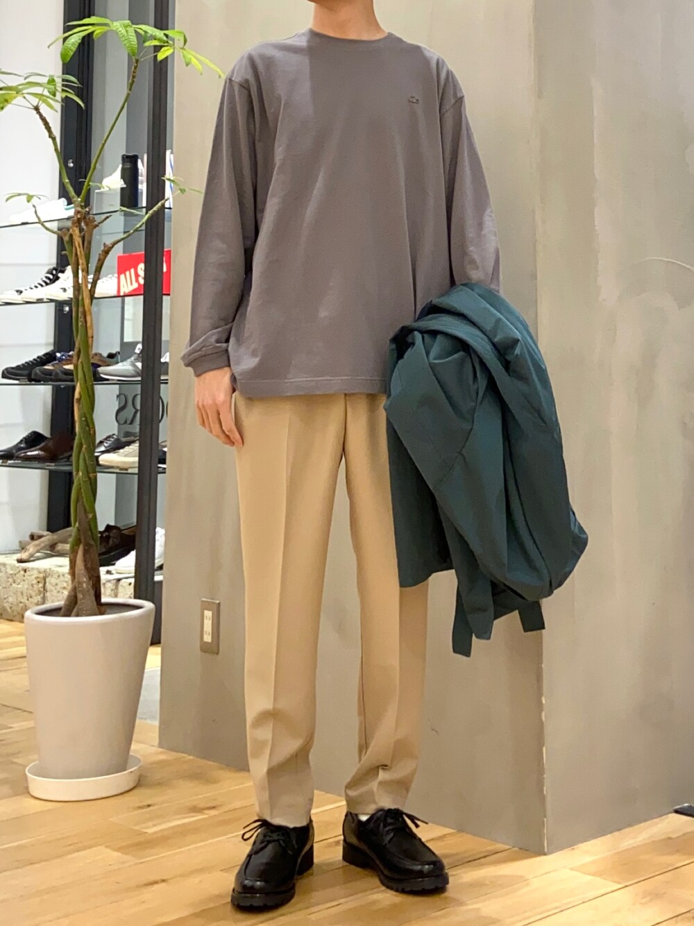 グリーン系のステンカラーコート、グレー系のTシャツ/カットソー、ベージュ系のその他パンツを着用したメンズの春コーディネートの2枚目の写真