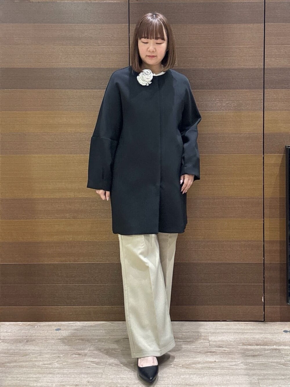 ブラック系のノーカラーコート、ベージュ系のその他パンツ、ホワイト系のハンドバッグを着用したレディースの冬コーディネートの6枚目の写真