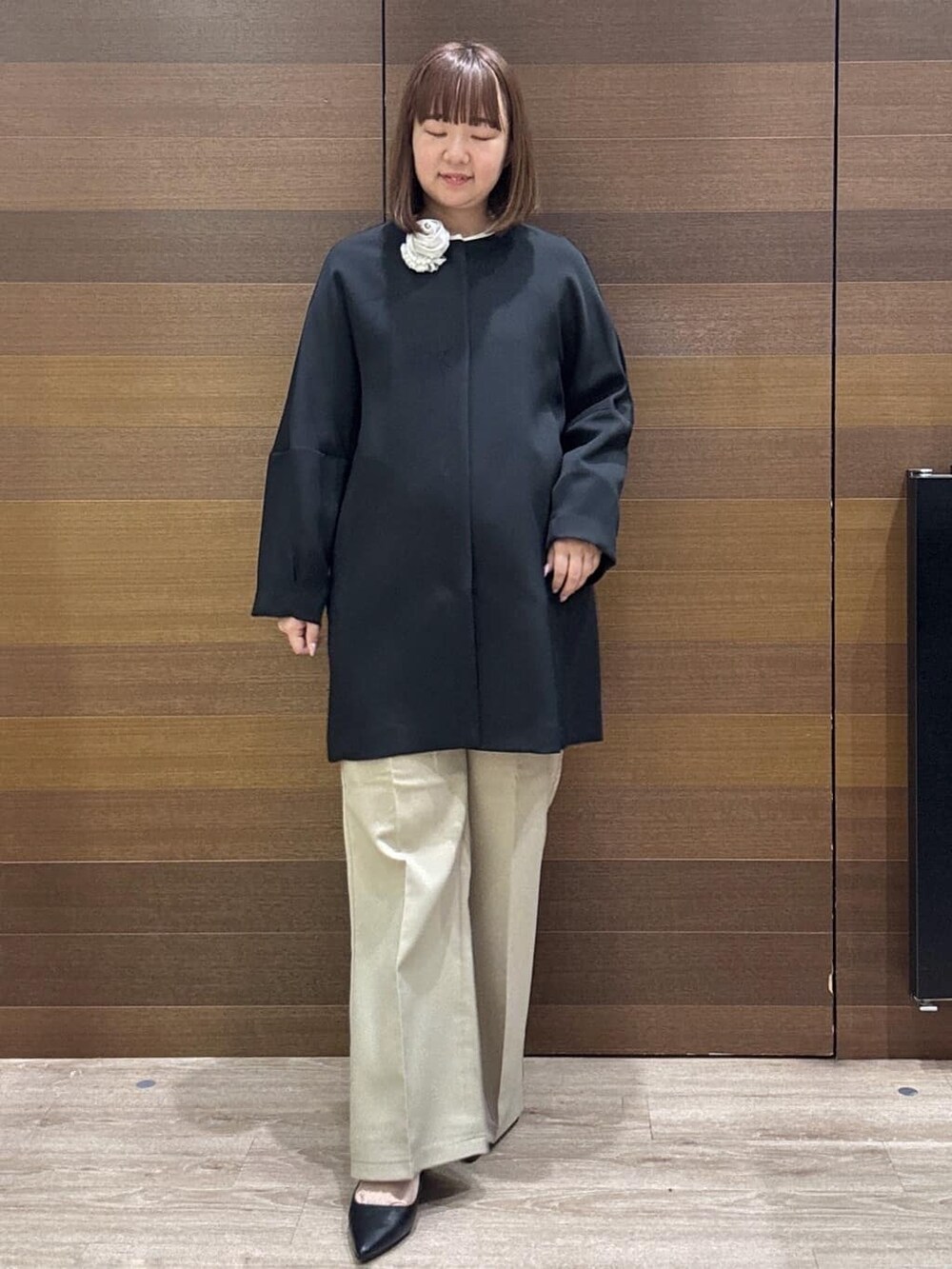 ブラック系のノーカラーコート、ベージュ系のその他パンツ、ホワイト系のハンドバッグを着用したレディースの冬コーディネートの2枚目の写真