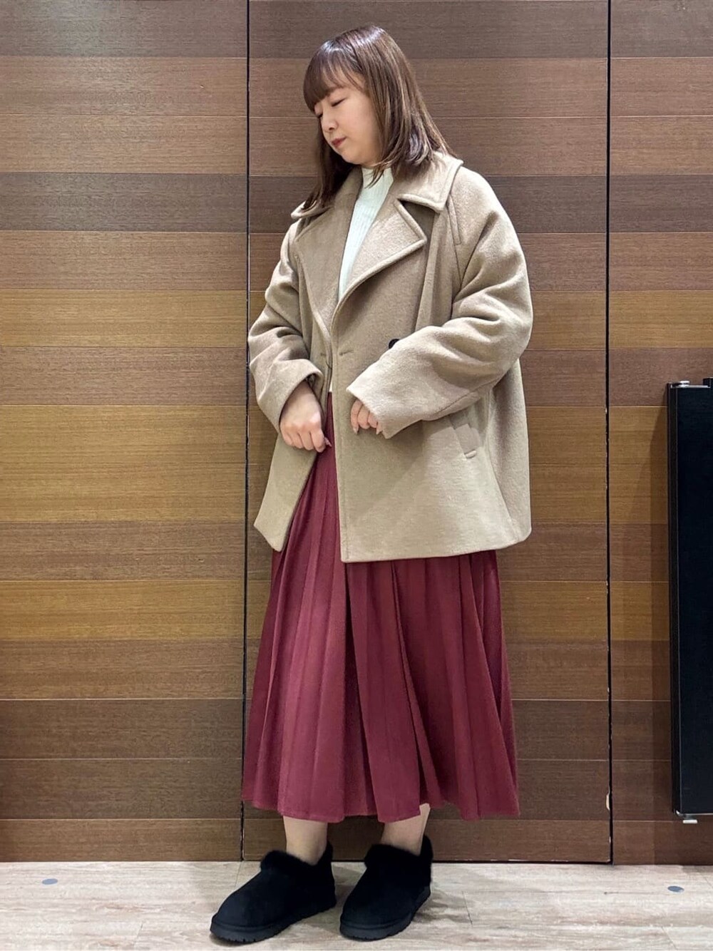 ベージュ系のピーコート、ホワイト系のニット/セーター、レッド系のスカートを着用したレディースの冬コーディネートの2枚目の写真