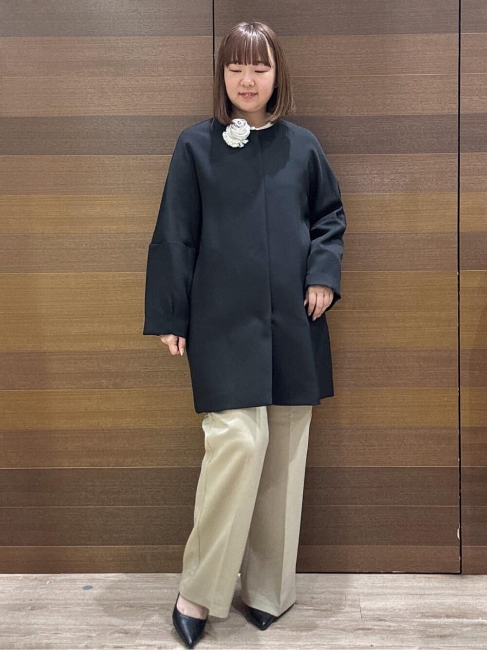ブラック系のノーカラーコート、ベージュ系のその他パンツ、ホワイト系のハンドバッグを着用したレディースの冬コーディネートの3枚目の写真