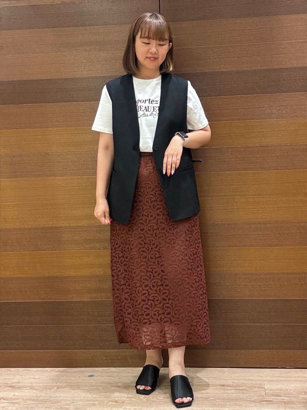 ブラック系のベスト、ホワイト系のTシャツ/カットソー、ブラウン系のスカートを着用したレディースの夏コーディネートの2枚目の写真