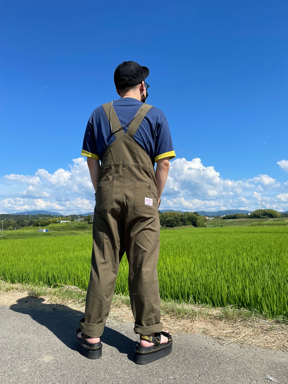 ブルー系のTシャツ/カットソー、グリーン系のサロペット/オーバーオール、ブラック系のサンダルを着用したメンズの夏コーディネートの2枚目の写真