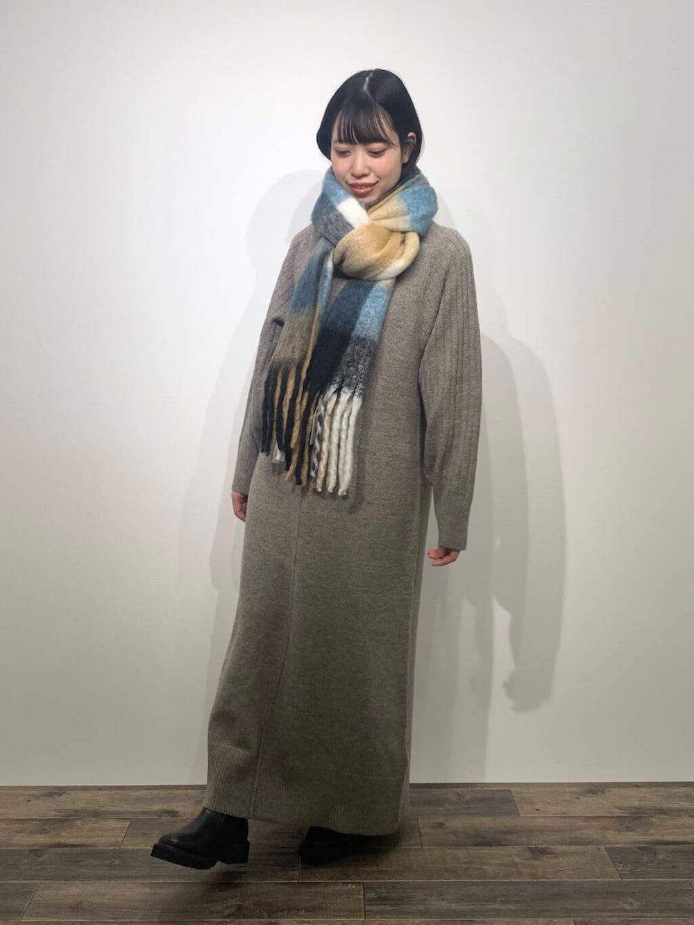 ブラック系のブーツ、ブラウン系のワンピース、ブルー系のマフラーを着用したレディースの秋コーディネートの2枚目の写真