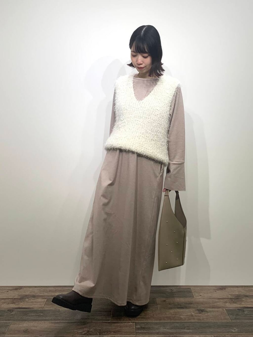 ベージュ系のトートバッグ、ブラウン系のブーツ、ホワイト系のベストを着用したレディースの秋コーディネートの2枚目の写真