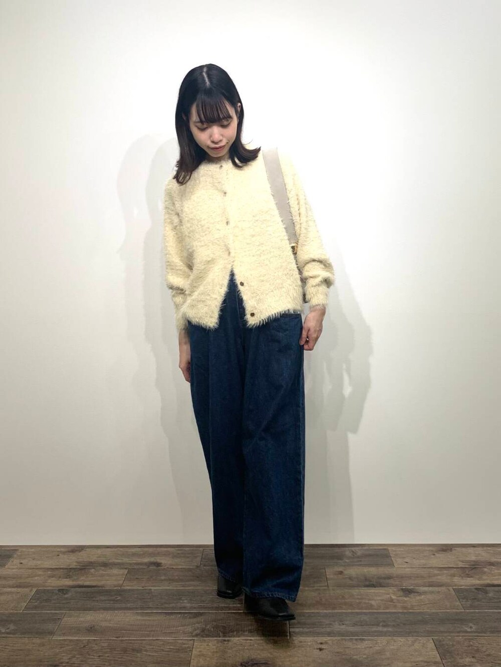 ブルー系のデニムパンツ、ベージュ系のハンドバッグ、ブラック系のブーツを着用したレディースの秋コーディネートの2枚目の写真