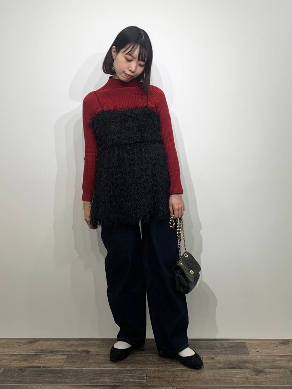 レッド系のニット/セーター、ブラック系のショルダーバッグ、ブルー系のデニムパンツを着用したレディースの冬コーディネートの3枚目の写真