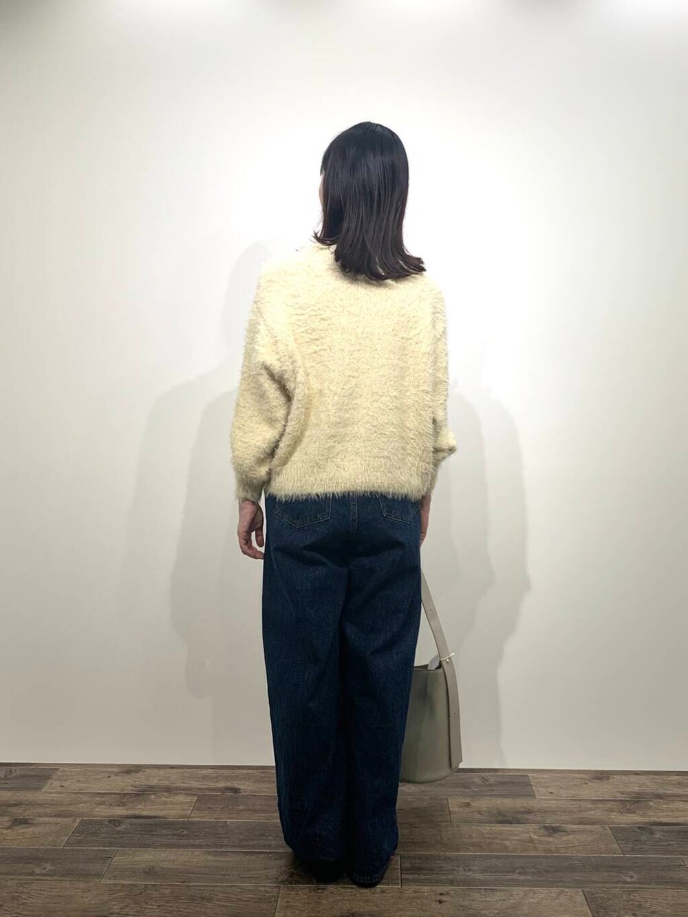 ブルー系のデニムパンツ、ベージュ系のハンドバッグ、ブラック系のブーツを着用したレディースの秋コーディネートの4枚目の写真