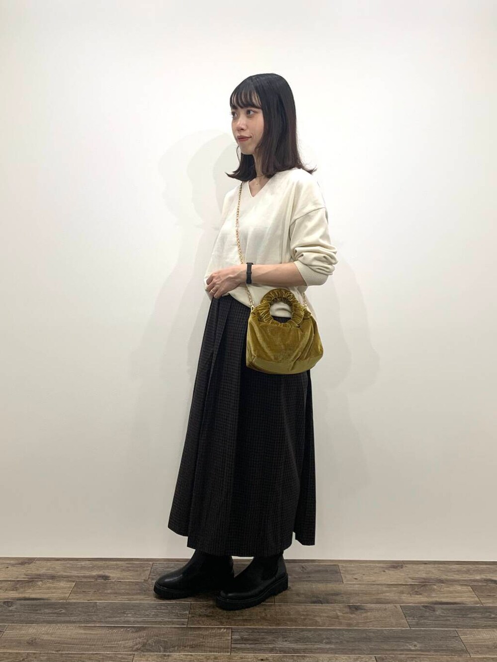 イエロー系のハンドバッグ、ブラック系のブーツ、ホワイト系のニット/セーターを着用したレディースの秋コーディネートの4枚目の写真