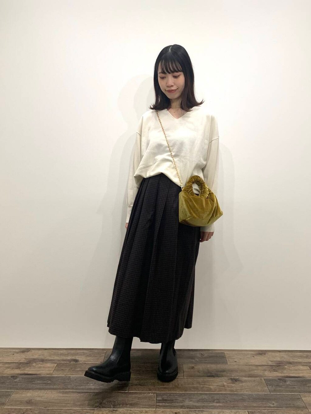 イエロー系のハンドバッグ、ブラック系のブーツ、ホワイト系のニット/セーターを着用したレディースの秋コーディネートの2枚目の写真