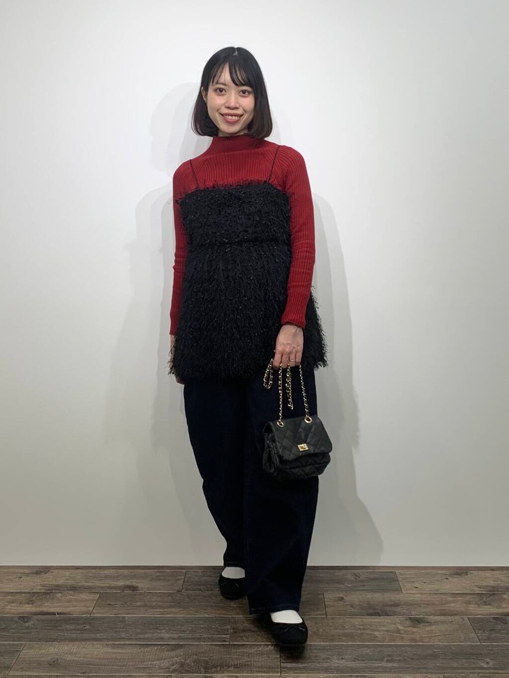 レッド系のニット/セーター、ブラック系のショルダーバッグ、ブルー系のデニムパンツを着用したレディースの冬コーディネートの2枚目の写真