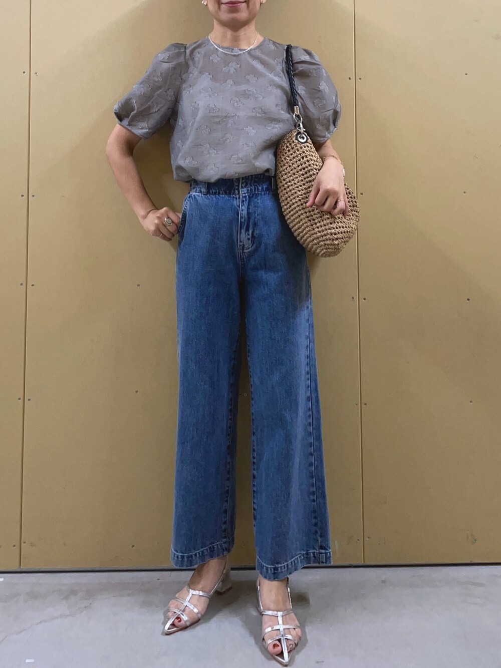 シルバー系のサンダル、ブルー系のデニムパンツ、ブラウン系のかごバッグを着用したレディースの夏コーディネートの2枚目の写真