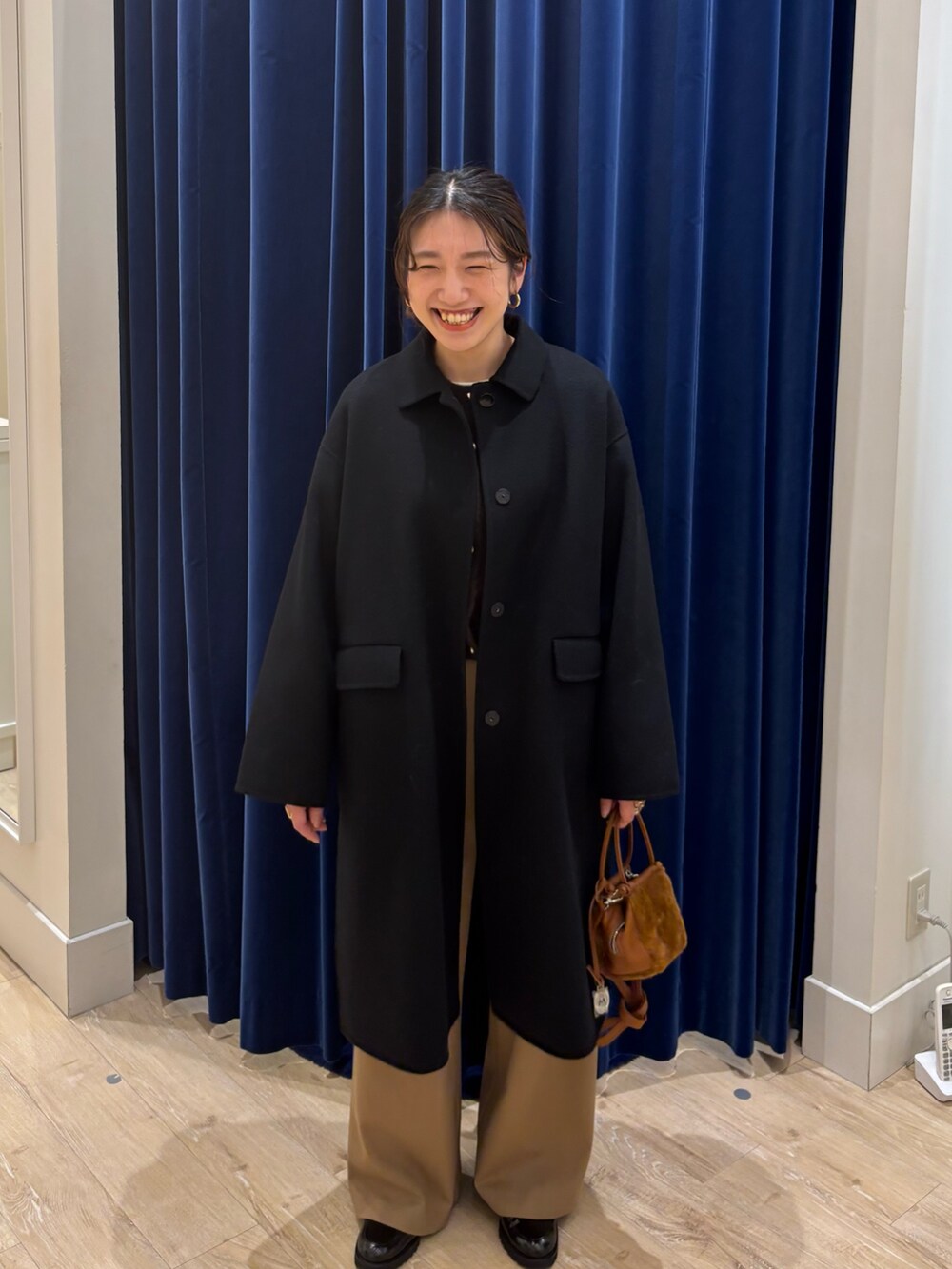 ブラック系のステンカラーコート、ブラウン系のカーディガン/ボレロ、イエロー系のその他パンツを着用したレディースの秋コーディネートの2枚目の写真