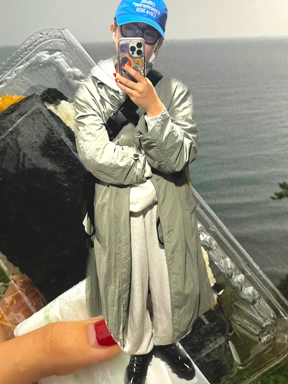 グリーン系のトレンチコート、ブラック系のスニーカー、ブルー系のキャップを着用したレディースの秋コーディネートの2枚目の写真