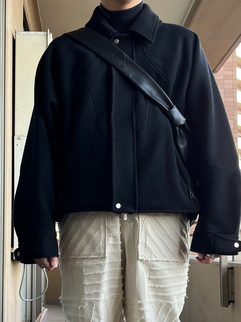 ブラック系のジャケット/アウター、ブラック系のショルダーバッグ、ホワイト系のパンツを着用したメンズの冬コーディネートの4枚目の写真