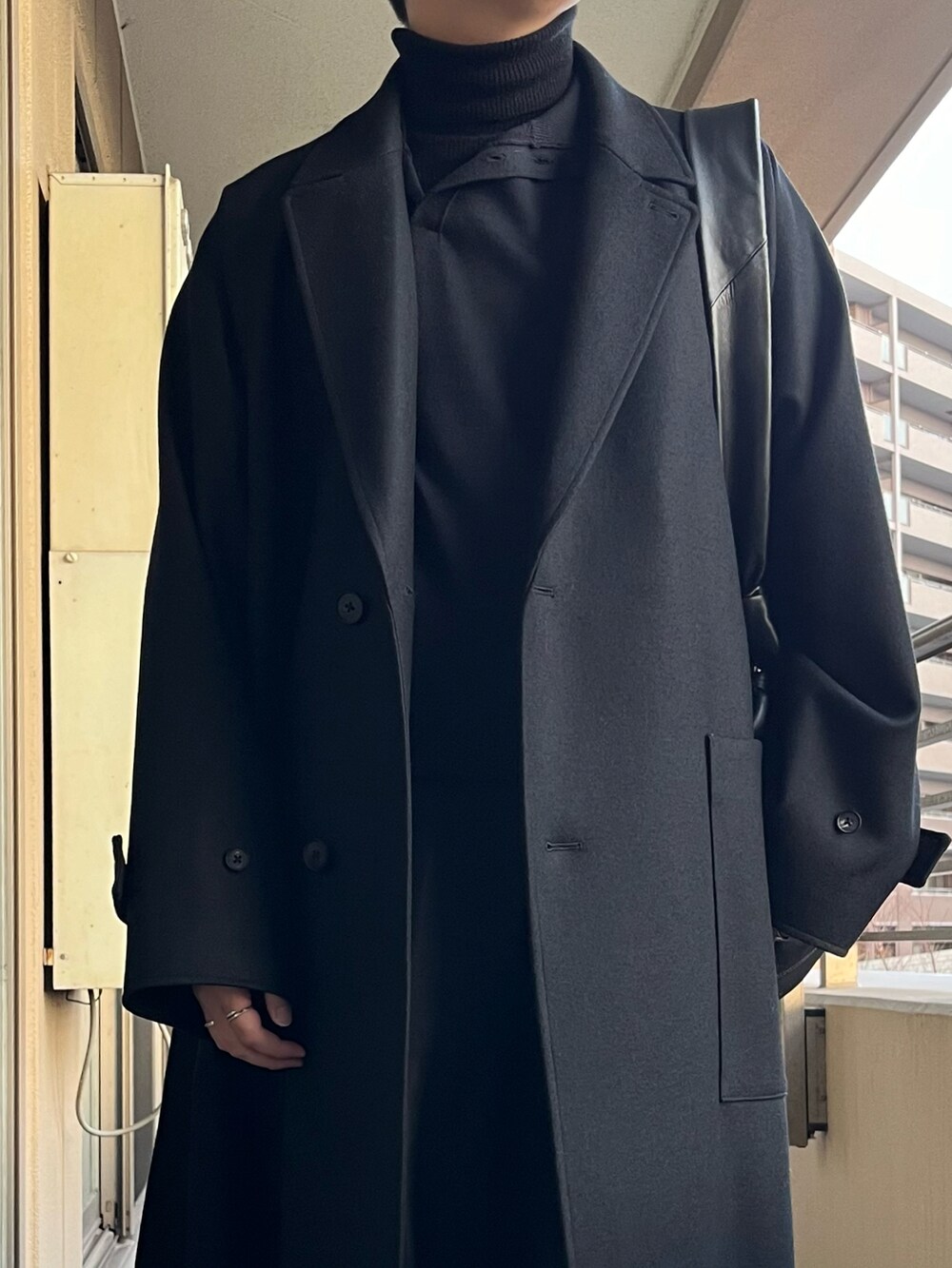 ブラック系のチェスターコート、ブルー系のニット/セーター、ブラック系のショルダーバッグを着用したメンズの冬コーディネートの5枚目の写真