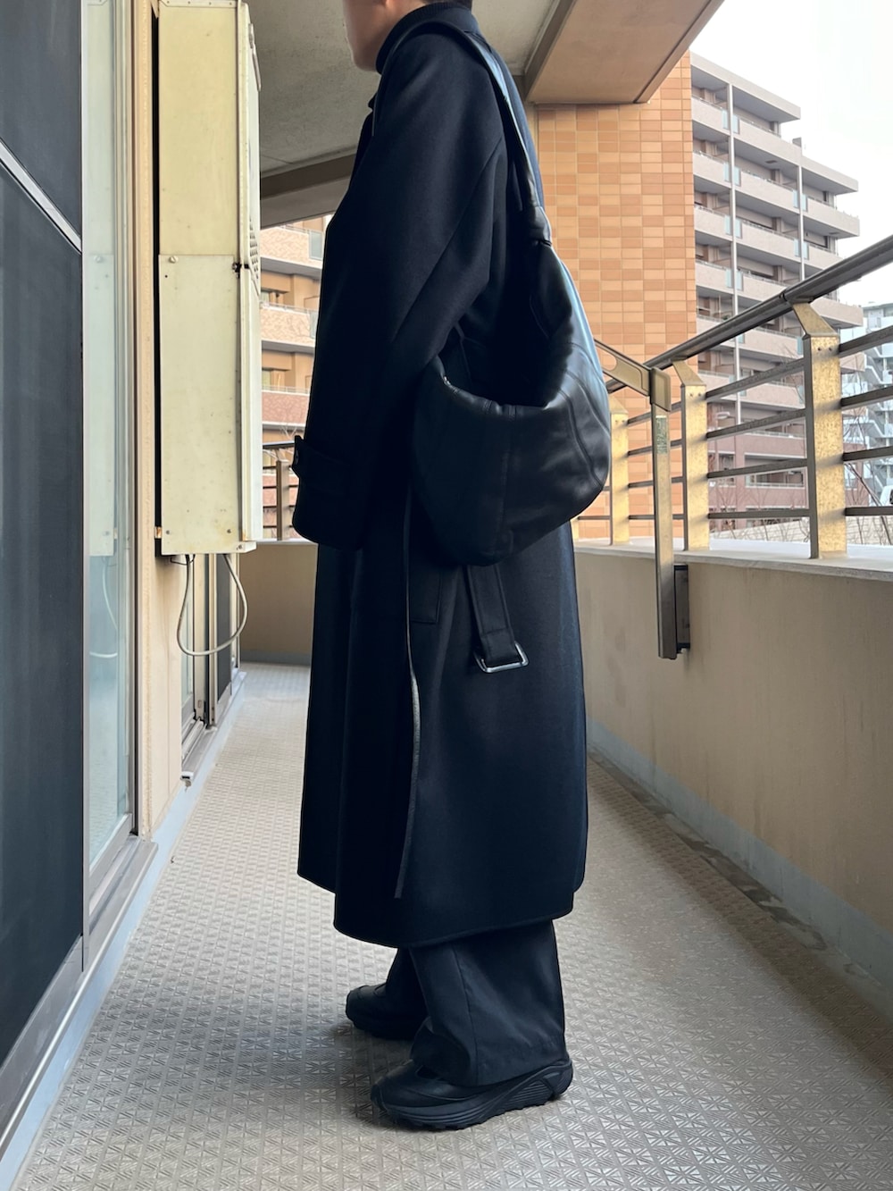 ブラック系のチェスターコート、ブルー系のニット/セーター、ブラック系のショルダーバッグを着用したメンズの冬コーディネートの3枚目の写真