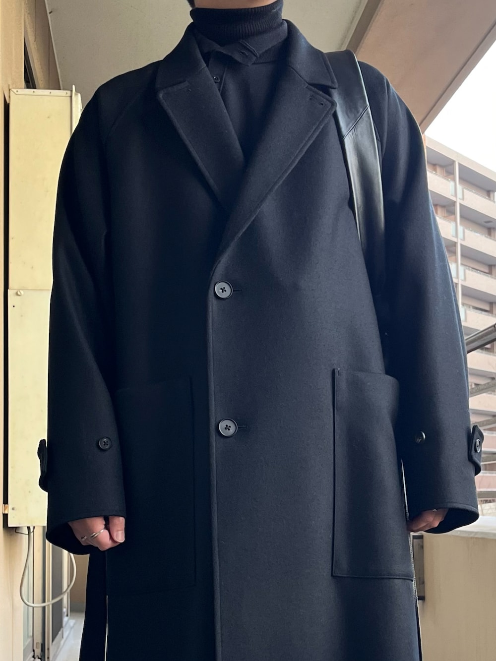 ブラック系のチェスターコート、ブルー系のニット/セーター、ブラック系のショルダーバッグを着用したメンズの冬コーディネートの4枚目の写真