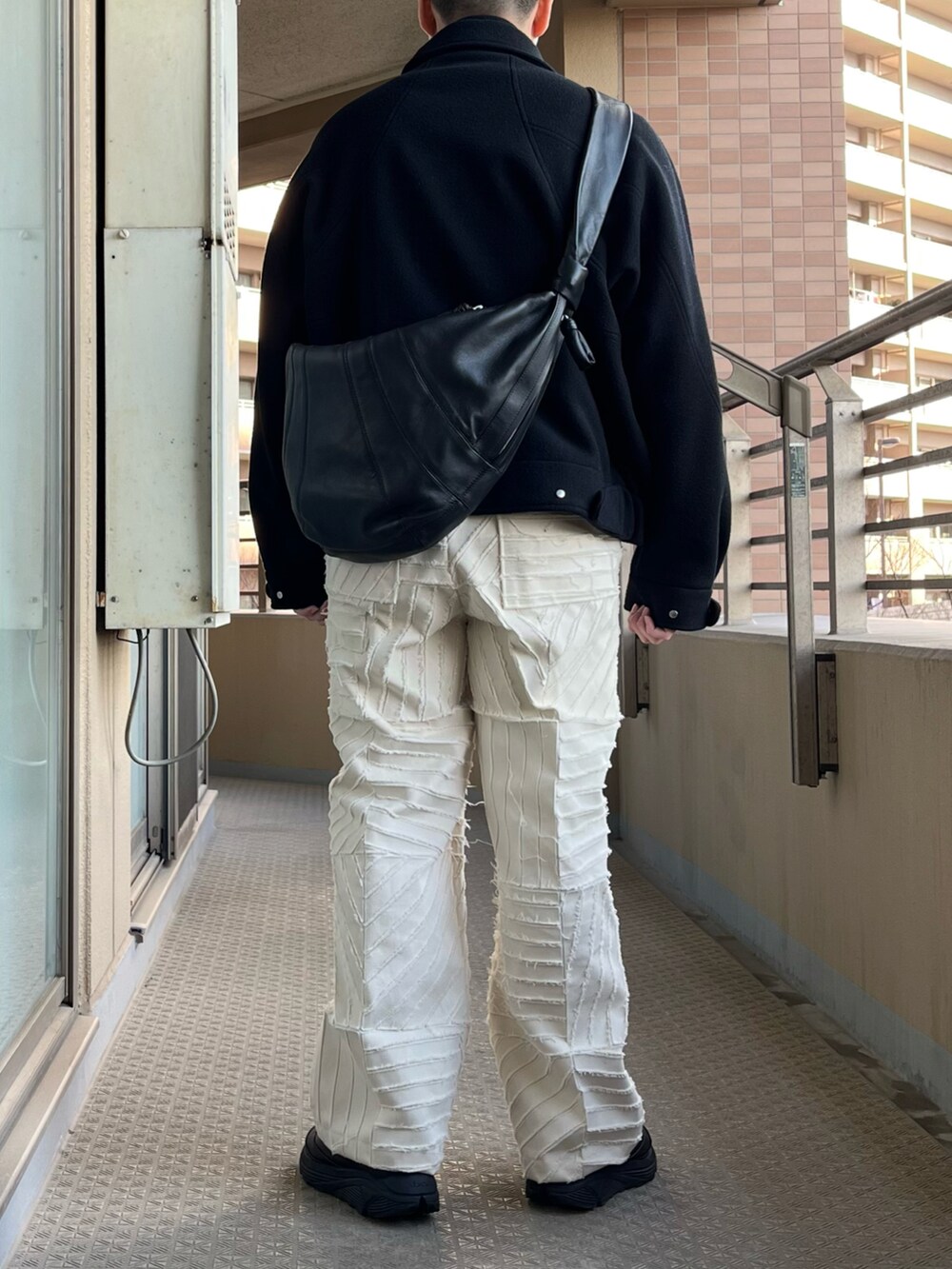 ブラック系のジャケット/アウター、ブラック系のショルダーバッグ、ホワイト系のパンツを着用したメンズの冬コーディネートの2枚目の写真