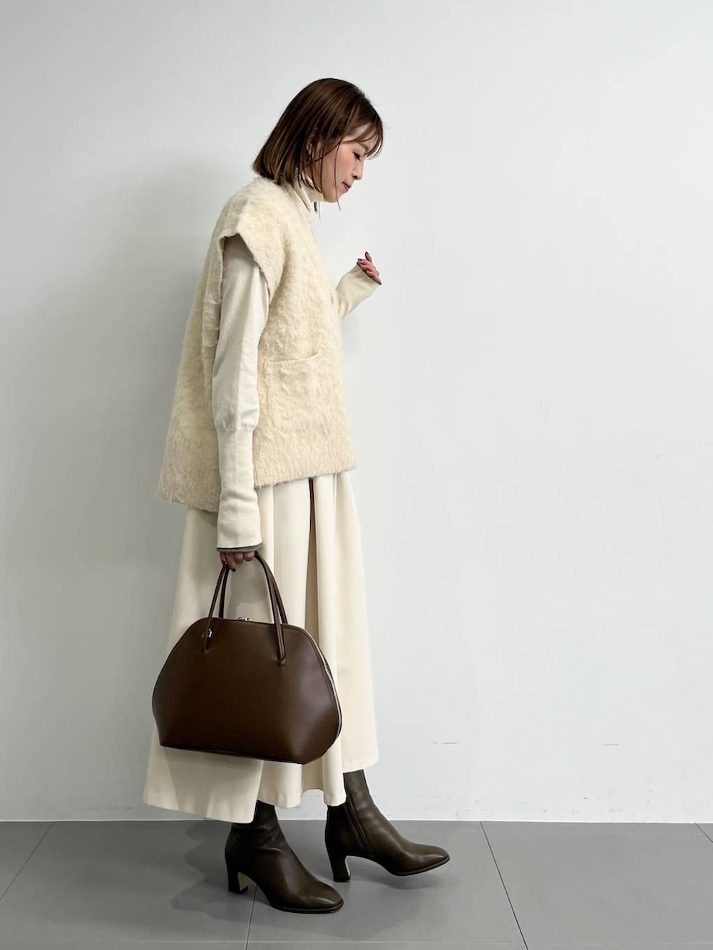 ブラウン系のトートバッグ、ブラウン系のブーツ、ホワイト系のニット/セーターを着用したレディースの冬コーディネートの2枚目の写真