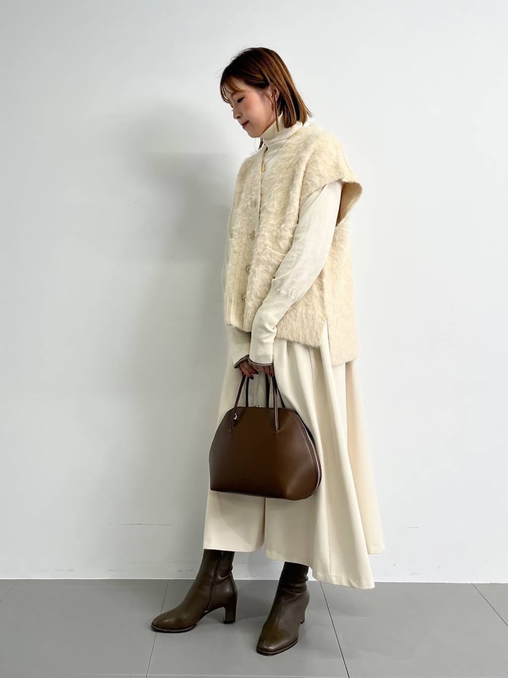 ブラウン系のトートバッグ、ブラウン系のブーツ、ホワイト系のニット/セーターを着用したレディースの冬コーディネートの4枚目の写真