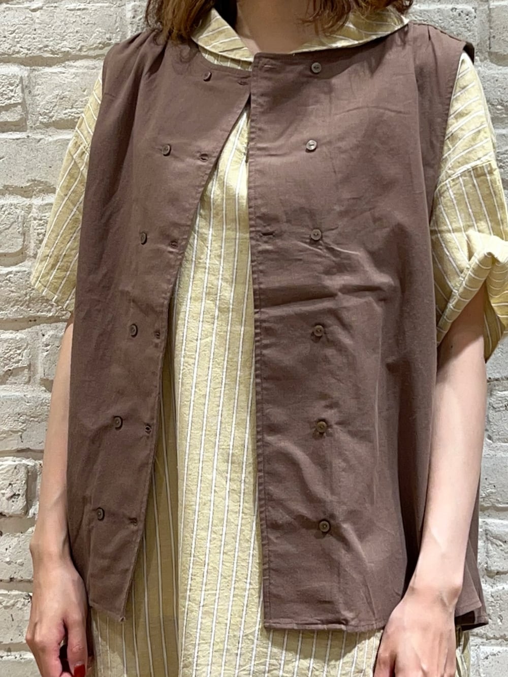 ホワイト系のタンクトップ、ブラウン系のベスト、イエロー系のチュニックを着用したレディースの夏コーディネートの3枚目の写真