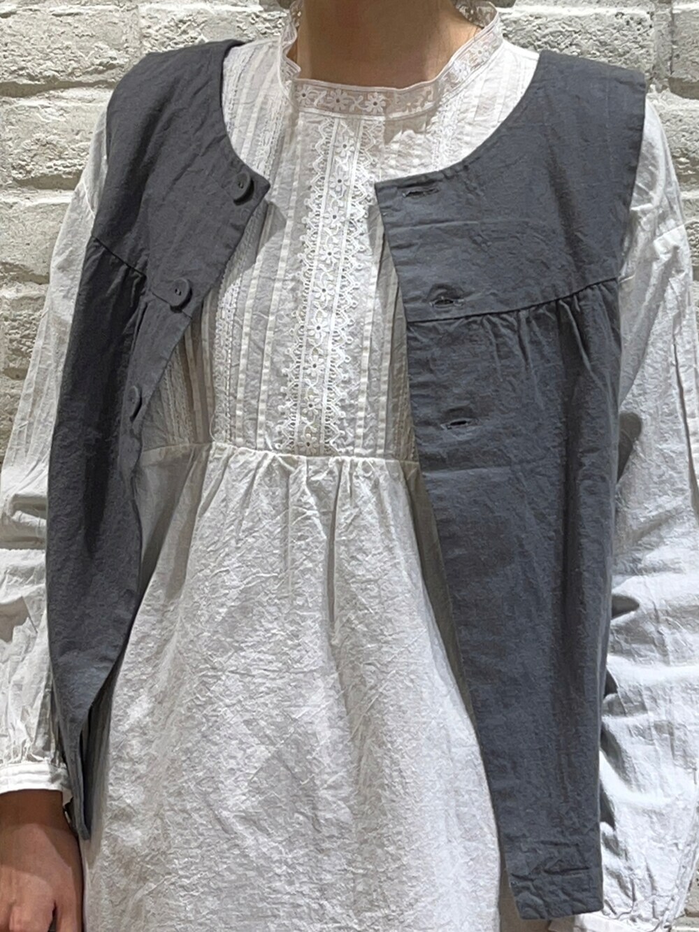 グリーン系のベスト、ホワイト系のシャツ/ブラウス、ブラック系のかごバッグを着用したレディースの春コーディネートの2枚目の写真