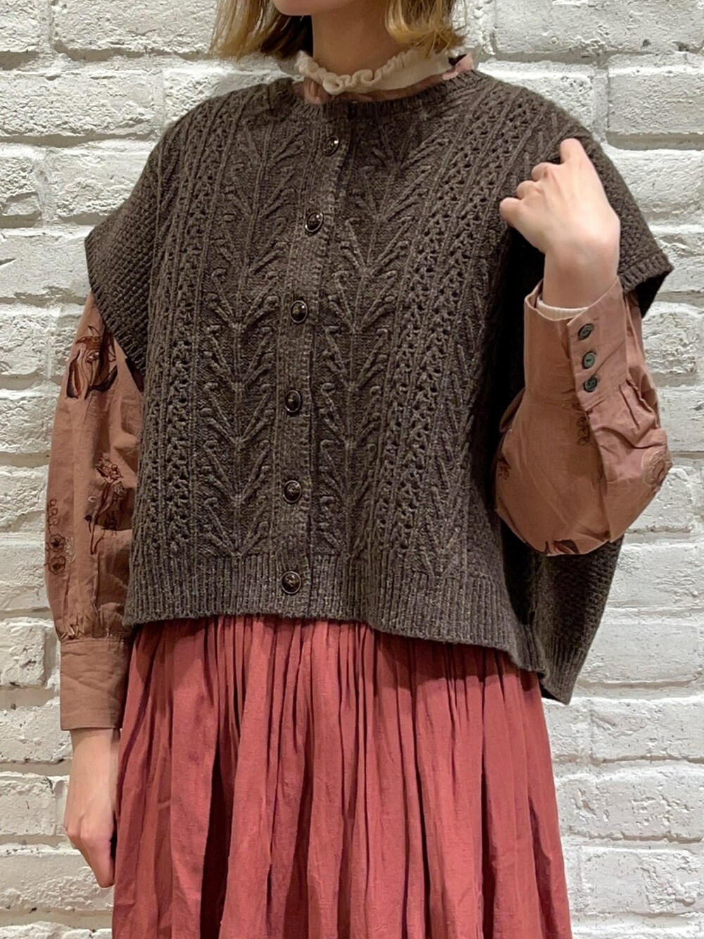 ホワイト系のニット/セーター、ブラウン系のベスト、レッド系のスカートを着用したレディースの秋コーディネートの2枚目の写真